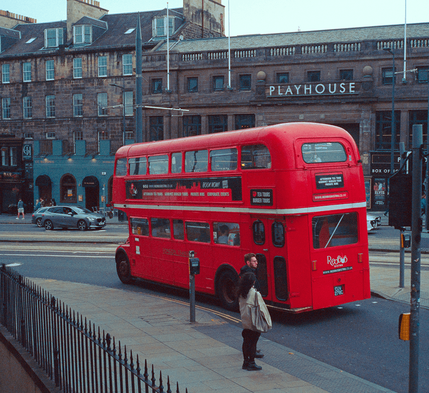 Red double-decker bus travelling through an Edinburgh street